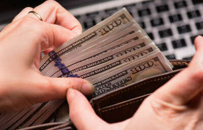 Close up of female hands counting US dollar banknotes at the table in front a laptop computer. Woman accountant with money and notebook.
