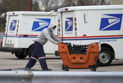 FILE - A United States Postal Service employee works outside a post office in Wheeling, Ill., Dec. 3, 2021. Four environmental groups that want the U.S. Postal Service to buy more electric delivery vehicles are suing to halt further purchases. The lawsuit, filed Thursday, April 28, 2022, in federal court in California, asks a judge to order the Postal Service to conduct a more thorough environmental review before moving forward with the next-generation vehicle program. (AP Photo/Nam Y. Huh, File)