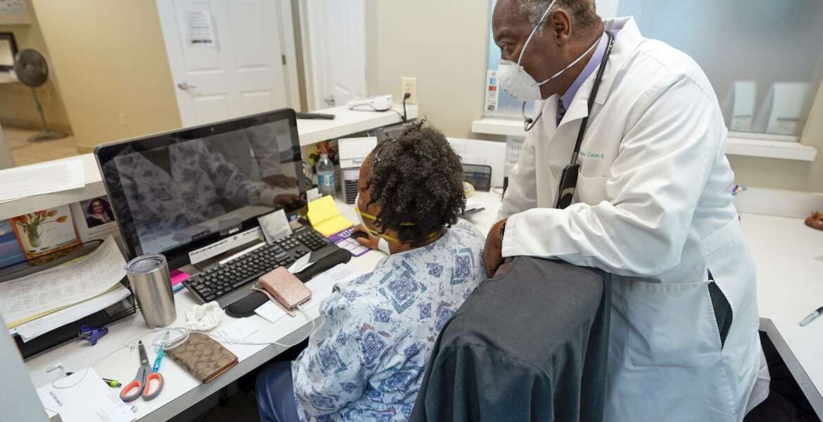 Dr. Rogers Cain, right, a primary care doctor, confers with office manager Cassandra Robinson, at his practice, Wednesday, Aug. 11, 2021, in Jacksonville, Fla. Cain said it was easier to convince his elderly patients to get the vaccine but his patients under the age of 50 remain skeptical. (AP Photo/John Raoux)